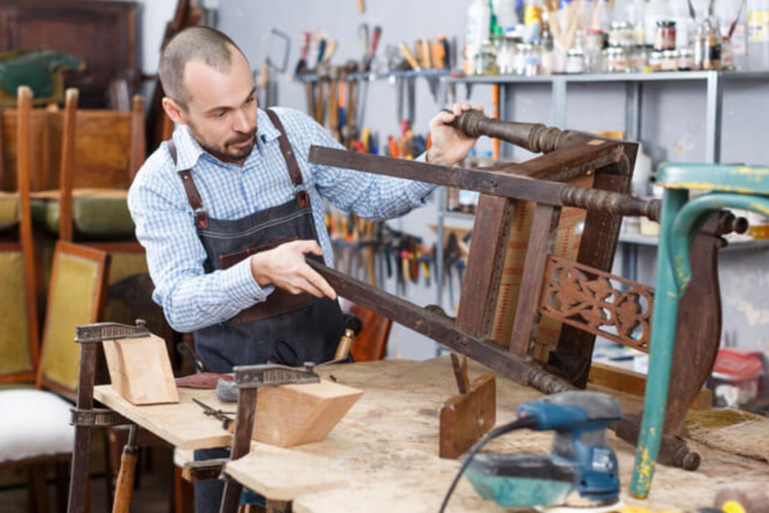A man is focused on crafting a wooden chair in a well-lit workshop, surrounded by tools and wood materials.