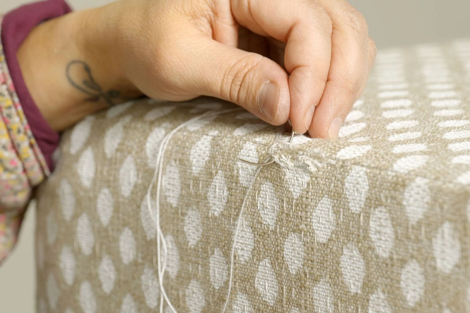 A person seated on a chair, focused on sewing with a needle and thread in hand.