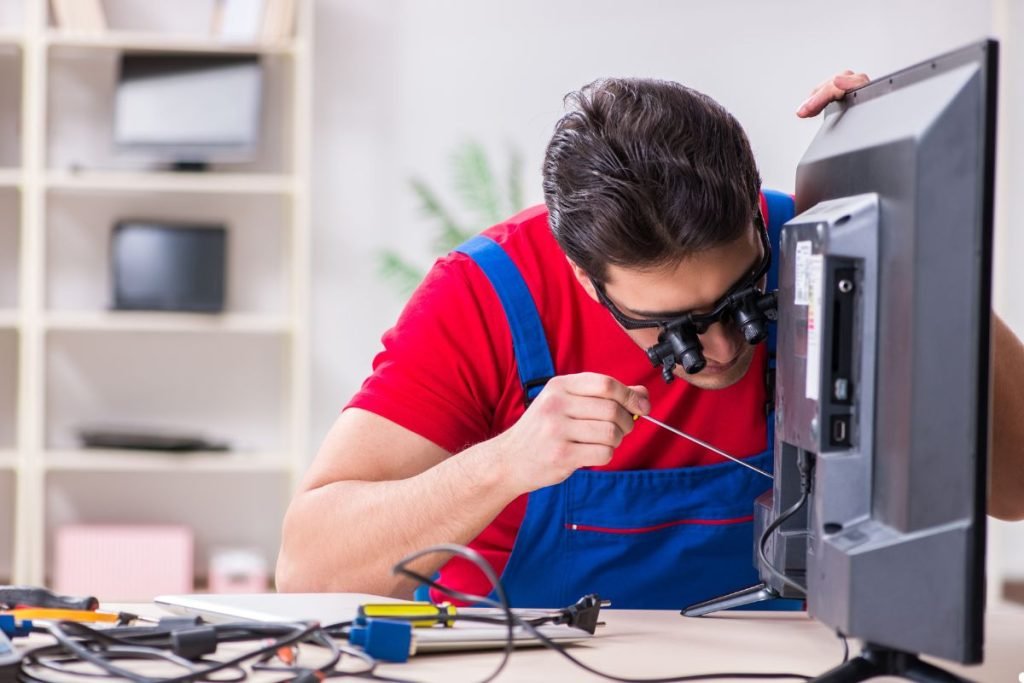 A man wearing an apron is repairing a computer, focused on the internal components.