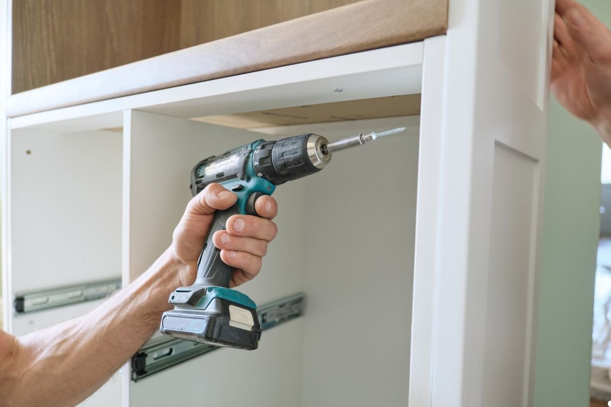 A man operates a drill while installing a cabinet, focused on securing it in place.