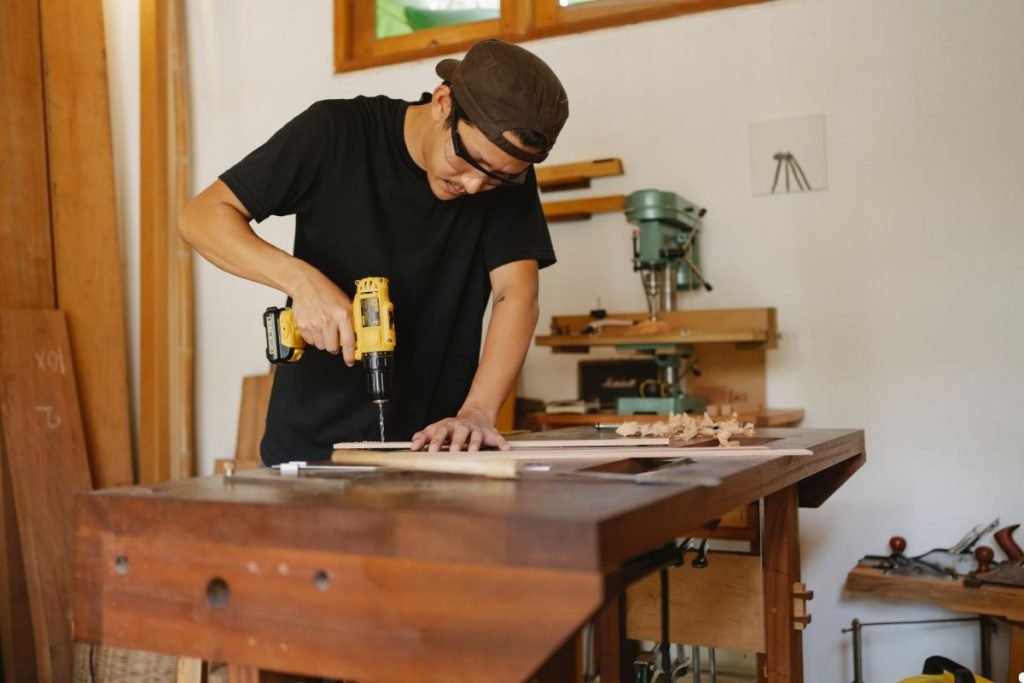 A man using a drill on a wooden table, focused on his task in a well-lit workspace.