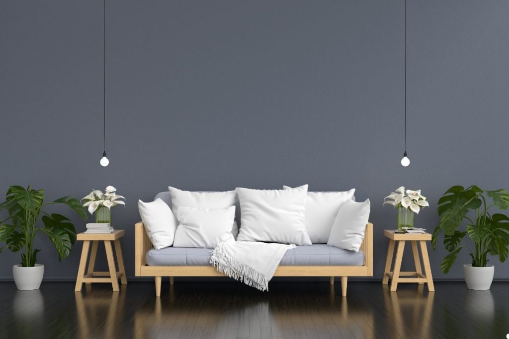 A wooden couch is positioned against a gray wall, accompanied by two potted plants, enhancing the room's natural ambiance.