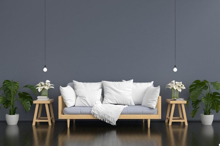 A wooden couch is positioned against a gray wall, accompanied by two potted plants, enhancing the room's natural ambiance.